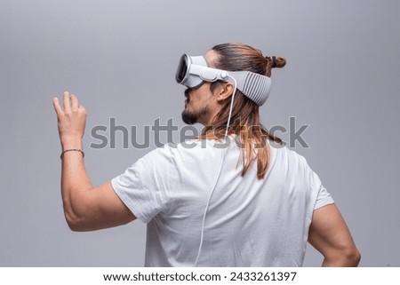 A young man engages with a virtual world using a mixed reality spacial computer headset, symbolizing cutting-edge technology in gaming and immersive digital experiences.  Royalty-Free Stock Photo #2433261397