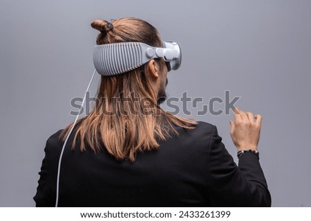 A young man engages with a virtual world using a mixed reality spacial computer headset, symbolizing cutting-edge technology in gaming and immersive digital experiences.  Royalty-Free Stock Photo #2433261399