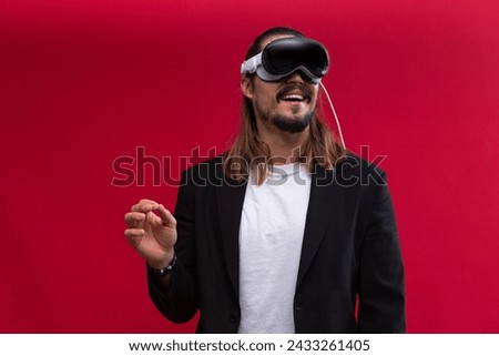 A confident man interacts with an augmented reality environment, showcasing the engaging world of spatial computing and AR and VR technology. Vivid red background Royalty-Free Stock Photo #2433261405