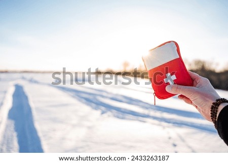 A red first aid kit in his hand against the background of snow, a hiking mini first aid kit, the glare of the sun against the background of winter. High quality photo
