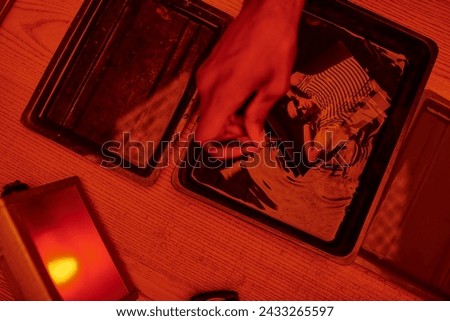 top view of photographer taking freshly developed photo paper in chemical solution with tweezers