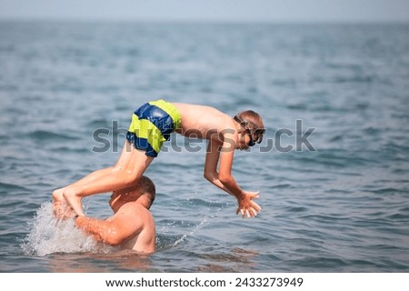 A man throws up a boy who dives into the sea on a sunny summer day