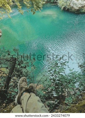 vertical photo. top view against the backdrop of a blue lake and feet in sneakers sitting on the top of the mountain. summer holiday concept. soft focus
