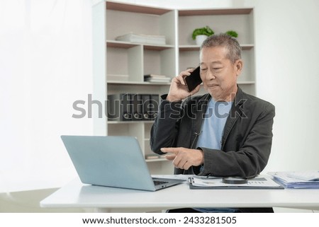 Senior Asian businessman uses smartphone to talk with customers Work on your laptop and discuss with clients about the requirements of a modern office or co-working space, startup.
