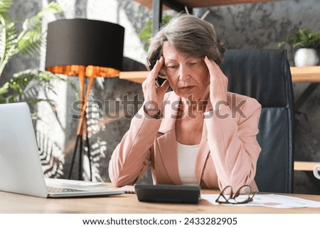 Sad tired caucasian senior businesswoman having headache suffering from migraine, rubbing her temples while working on laptop in office. Debt loan mortgage concept Royalty-Free Stock Photo #2433282905
