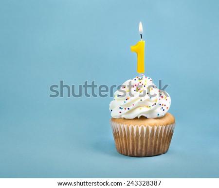 A birthday cup cake with buttercream icing,  sprinkles and a lit number one birthday candle. Royalty-Free Stock Photo #243328387
