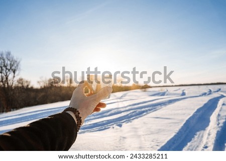 Hand holding cup of coffee on the background of the glare of the sun, winter landscape, drinking tea in nature, winter evening in the forest. High quality photo