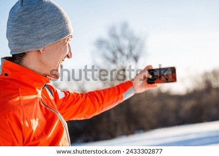Man taking selfie on phone while standing in winter forest, guy taking pictures of himself on smartphone, landscape photography. High quality photo