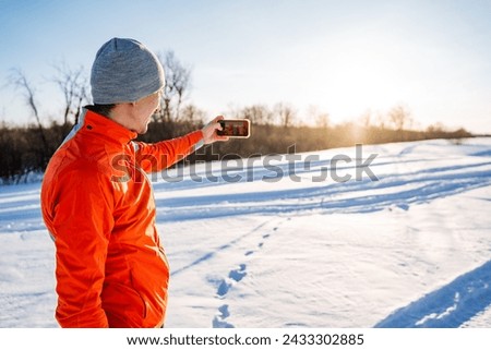 Man taking selfie on smartphone while standing on snow in winter forest, taking pictures of himself, self-portrait, winter outdoor recreation. High quality photo