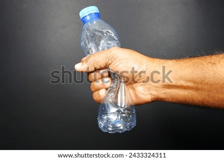 Crumbled a empty plastic water bottle by hand with black background close-up view, Water bottle crushed by hand closeup shot, No plastic concept photography  Royalty-Free Stock Photo #2433324311