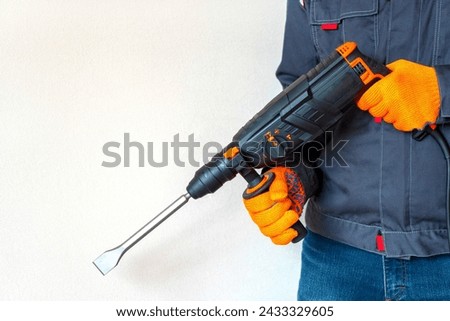  workman with a rotary hammer. Hands in protective gloves with hammer drill perforator. Copy space. Royalty-Free Stock Photo #2433329605