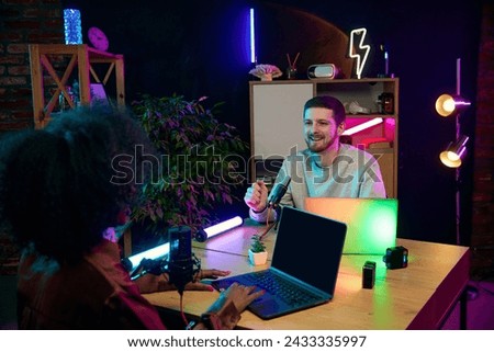 Young people, man and woman, influencers sitting at table with microphone and laptops, talking, recording online interview, podcast. Concept of online communication, modern technology, mass media
