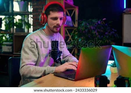 Young man, journalist, influencer sitting in home office with microphone and laptop, recording online interview. Social media podcast. Concept of online communication, modern technology, mass media