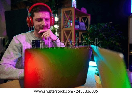 Young smiling man sitting in home office with microphone and laptop, leading online interview. Social media influencer podcast. Concept of online communication, modern technology, mass media