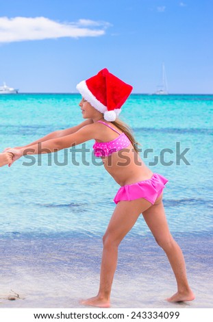 Little adorable girl in red Santa hat at tropical beach