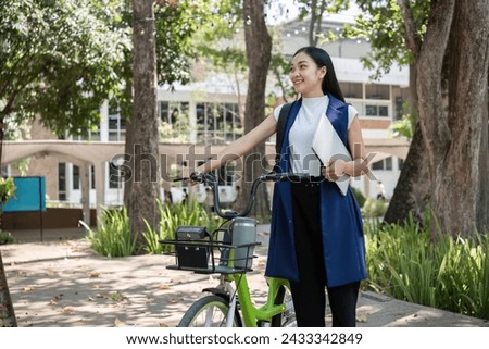 A young Asian woman commutes to work by cycling in a green city, carrying a backpack and using a reusable drinking cup to avoid harming the environment.