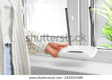 Woman with wi-fi router near window at home, closeup Royalty-Free Stock Photo #2433347689