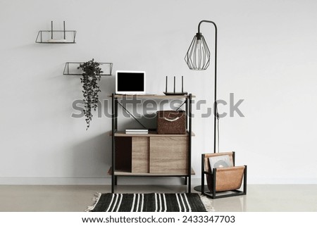 Modern wi-fi router with laptop on shelf near light wall in interior of room Royalty-Free Stock Photo #2433347703