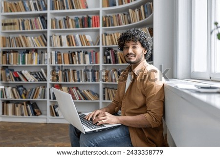 An engaged young adult sits comfortably in a well-lit space, surrounded by books, focused on work being done on a laptop. Setting suggests a modern library or a study room with a peaceful atmosphere.