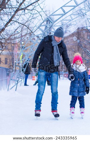 Young father and adorable little girl on skating rink outdoor