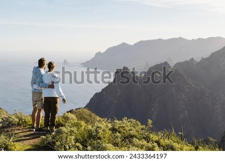 Couple of traveler in love enjoying vacation in nature. Hikers watching beautiful coastal scenery. Tenerife, Canary Islands, Anaga Rural Park, Spain. Travel, Outdoors and Lifestyle Concept.