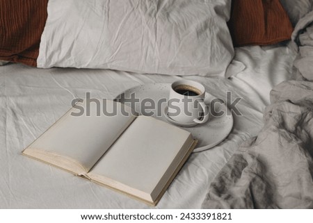 Cup of coffee, open books on white bed sheet. Breakfast in bed concept. Blurred muslin, linen pillows, blanket. Moody cozy Scandinavian bedroom. Top view, no people, lifestyle banner.