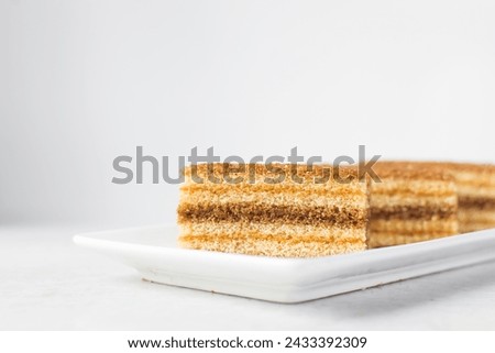 slice of vanilla cake with jam filling on a white plate, thin layers of vanilla and chocolate cake with jam filling on a white background Royalty-Free Stock Photo #2433392309