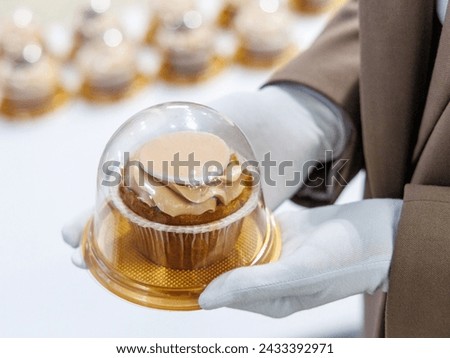 hands in white gloves give a cupcake in a plastic package