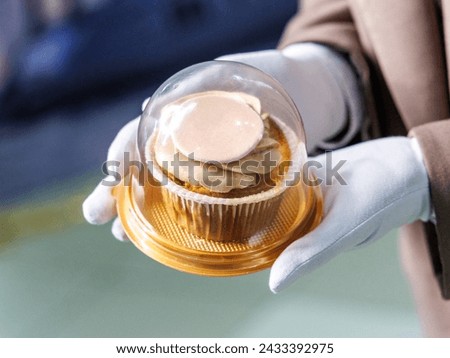 a girl in white gloves gives a delicious cupcake in a plastic package as a gift