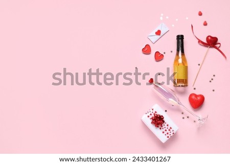Bottle of champagne with glass, gift box and decor on pink background. Valentine's Day celebration