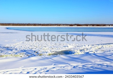 A river with the ice and snow. Cold water and the forest on the horizon. Winter landscape in cold frosty weather in daytime. Blue sky Beauty of nature