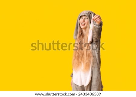 Beautiful young happy woman in bunny costume with decorative egg on yellow background. Easter celebration