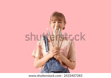 Female artist with paint brushes on pink background