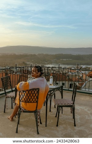 Vertical image of tranquil black woman smiling on a terrace at sunset overlooking a historical european town next to the river on a solo travel vacation.
