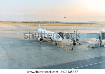 Passenger plane on the airfield connected to walkway.The gate sleeve is docked to the aircraft. Royalty-Free Stock Photo #2433435867