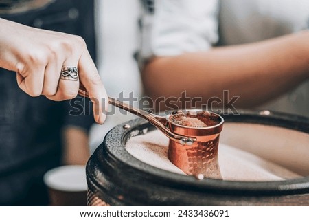 Woman's Hand Crafting Coffee in the Sands with a Steel Turkish Coffee Pot close up Royalty-Free Stock Photo #2433436091
