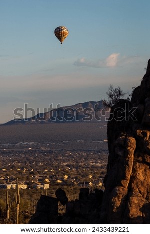 A colorful hot air balloon in the sky above the Sonoran Desert. Early morning adventure in a balloon floating past mountains and saguaro cacti near Tucson, Arizona in Pima County, USA. Royalty-Free Stock Photo #2433439221