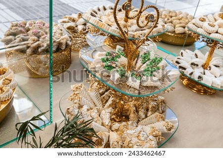 Horizontal photo a sumptuous display of Arabic sweets, featuring a variety of textures and flavors, presented on exquisite golden stands with intricate details. Food and culture concept. Royalty-Free Stock Photo #2433462467