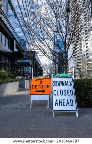 Street level of a modern downtown city during a building boom, sidewalk closed and detour signs for pedestrian safety during construction
