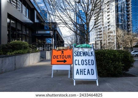 Street level of a modern downtown city during a building boom, sidewalk closed and detour signs for pedestrian safety during construction
