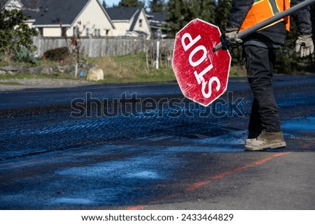Traffic control worker in orange reflective safety vest with temporary stop sign managing traffic in a road work construction zone

