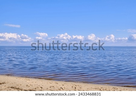 A tranquil seascape with gentle ripples on the water and billowy white clouds in the sky, their reflections dancing on the serene surface, creating a harmonious interplay of light and nature Royalty-Free Stock Photo #2433468831