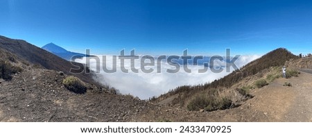 Panoramic view of Woman tourist visiting the island of Tenerife takes photographs from the top of the mountain above a sea of clouds, in the distance rises the Teide volcano