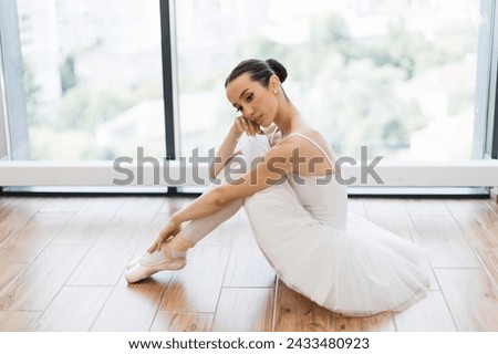 Side view portrait of talented ballerina finished her wonderful performance and resting while sitting at wooden floor, copy space. Beautiful young female ballet dancer relaxing after rehearsal. Royalty-Free Stock Photo #2433480923