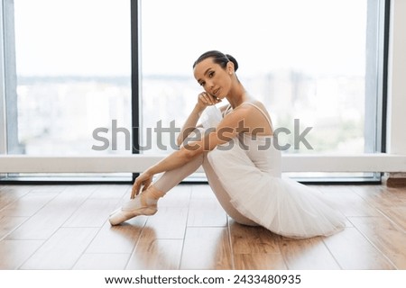 Side view portrait of talented ballerina finished her wonderful performance and resting while sitting at wooden floor, copy space. Beautiful young female ballet dancer relaxing after rehearsal. Royalty-Free Stock Photo #2433480935
