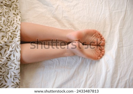 The child's bare feet sticking out from under the blanket. The kid sleeping kid on his stomach. Daytime sleep. Cozy and soft bed linen and mattress. Morning dream. Copy space. Happy childhood concept. Royalty-Free Stock Photo #2433487813
