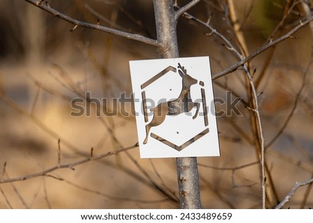 A sign with a wild animal on a white background among bushes at sunset contrasts with its surroundings.