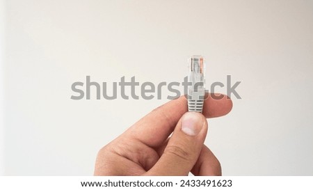 LAN ethernet cable in hand. Gray RJ45 twisted pair cable for computer network. Cat 5e UTP connection. White isolated background. Royalty-Free Stock Photo #2433491623