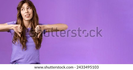 Unimpressed ignorant snobbish attractive curly-haired girl disagree lame idea look away disappointed show thumbs down dislike disapproval gesture not interested upset purple background. Royalty-Free Stock Photo #2433495103