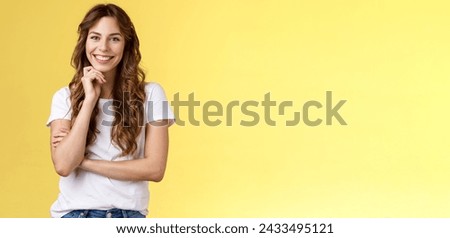 Tender feminine enthusiastic charming european woman curly long hairstyle laughing silly gaze grinning joyfully touch chin intrigued standing curious interested listening amused yellow background. Royalty-Free Stock Photo #2433495121